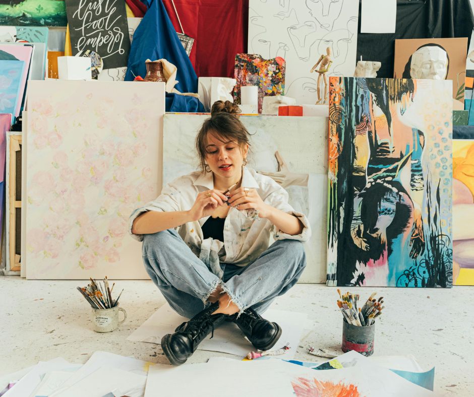 Person sitting among art supplies and artwork in a studio setting