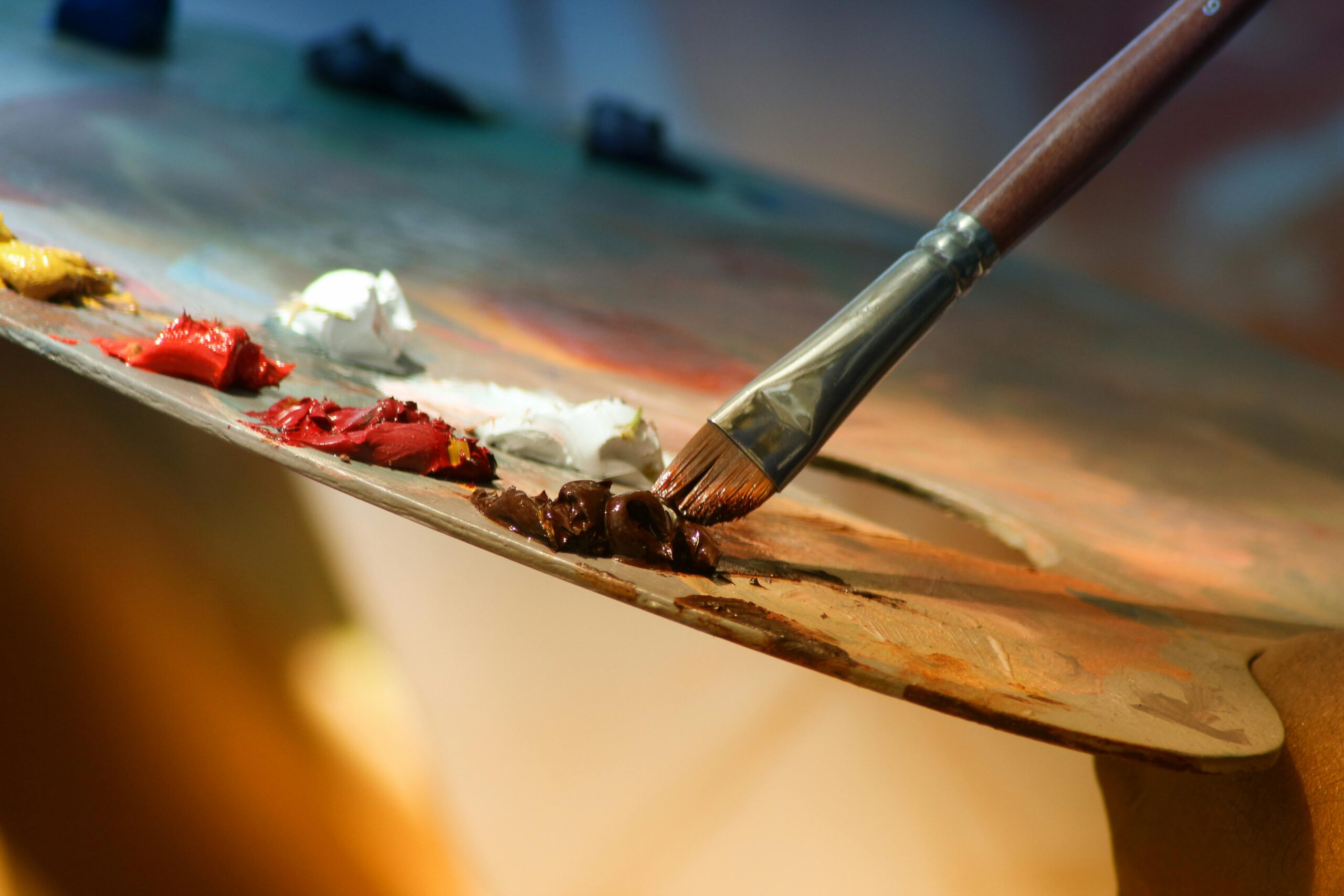 Paintbrush dipping into paint on a wooden palette with a blurred background